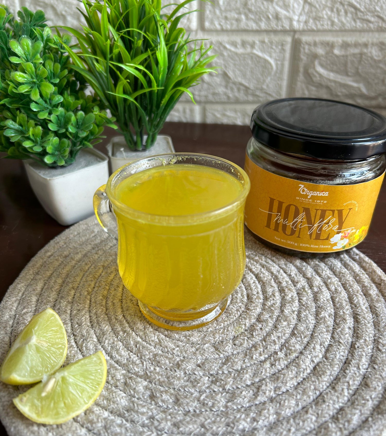 Glass of yellow liquid with a jar of honey and lime slices on a textured surface.